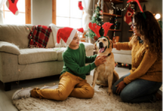 a teenager and a parent petting a dog wearing a Christmas outfit in decorated living room