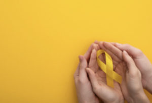 two pairs of hands holding a yellow ribbon on yellow background