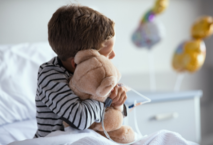 A kid hugging his teddy bear on hospital bed
